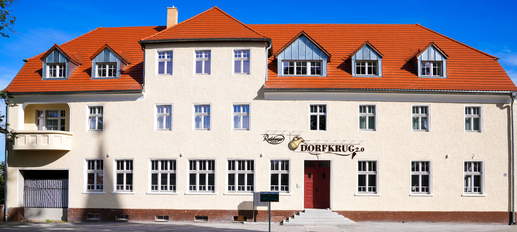Der sanierte Dorfkrug heute: helle Fassade, rotes Ziegeldach, rote Eingangstür