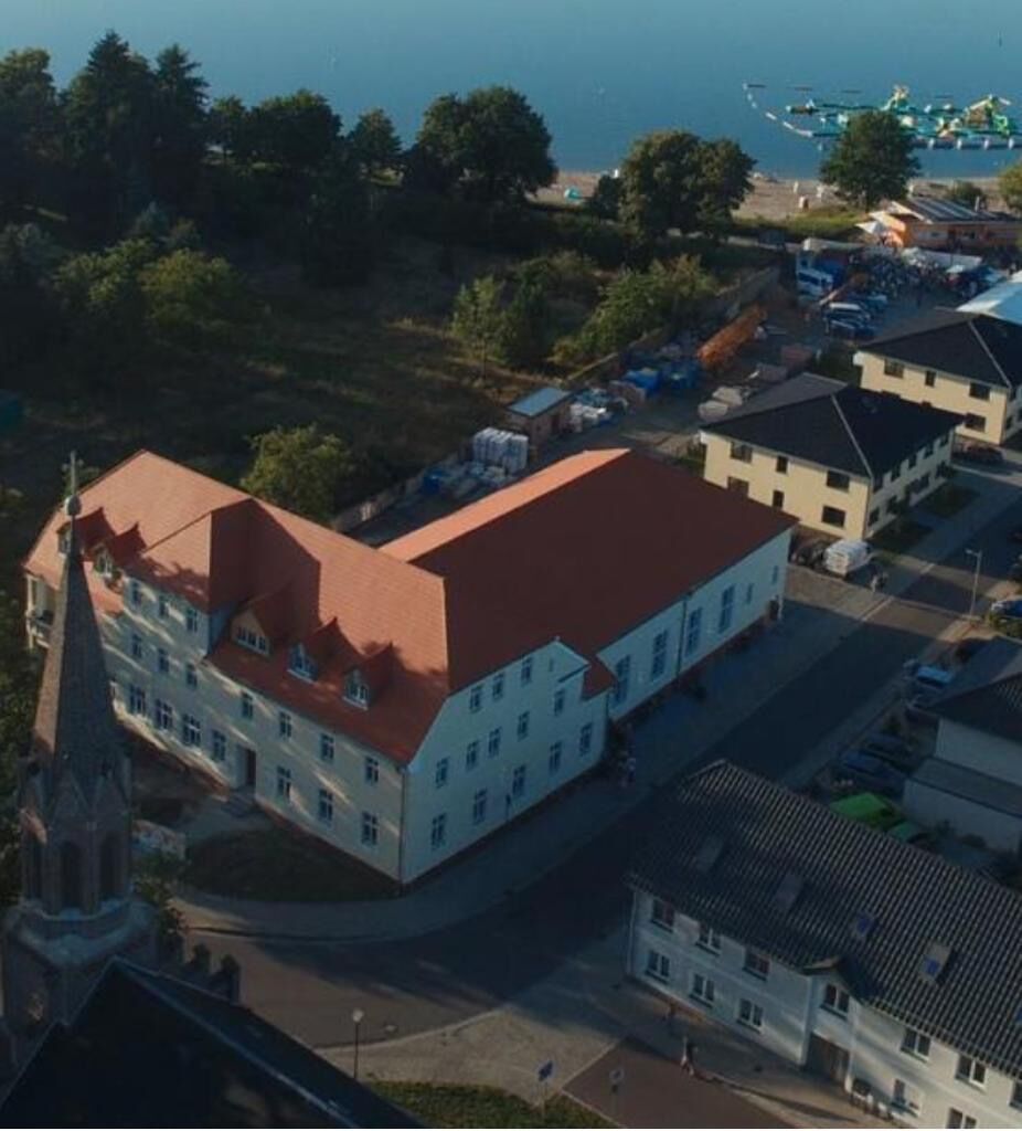 Luftbild: der Dorfkrug mit rotem Dach, dahinter Strand und Senftenberger See