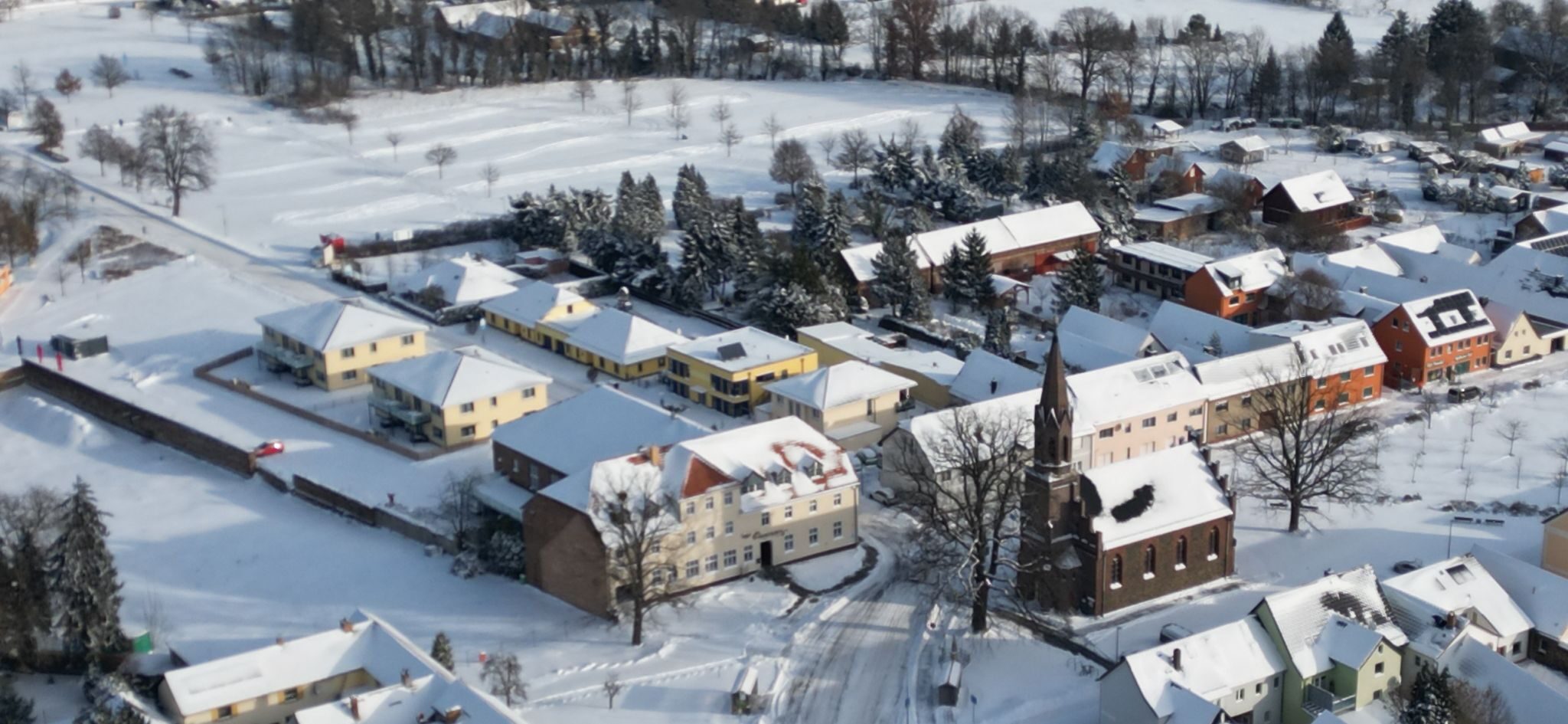 Luftbild von Großkoschen im Schnee: der Dorfkrug am Dorfanger neben der Kirche