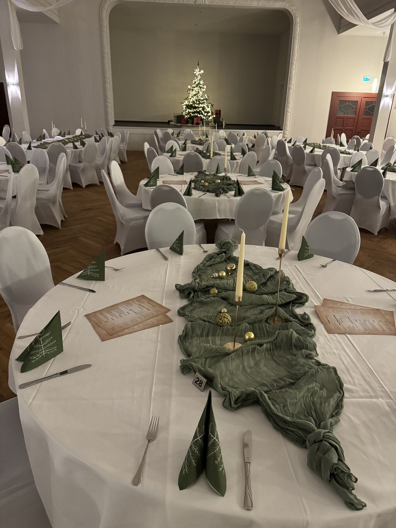 Weihnachtlich gedeckter Tisch im Saal, Tannenbaum auf der Bühne